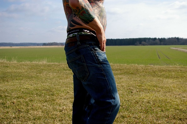 Shirtless man dressed in jeans standing on a meadow